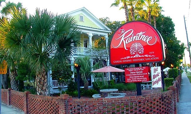 Sign for The Kaintree restaurant in a historic building surrounded by palm trees.