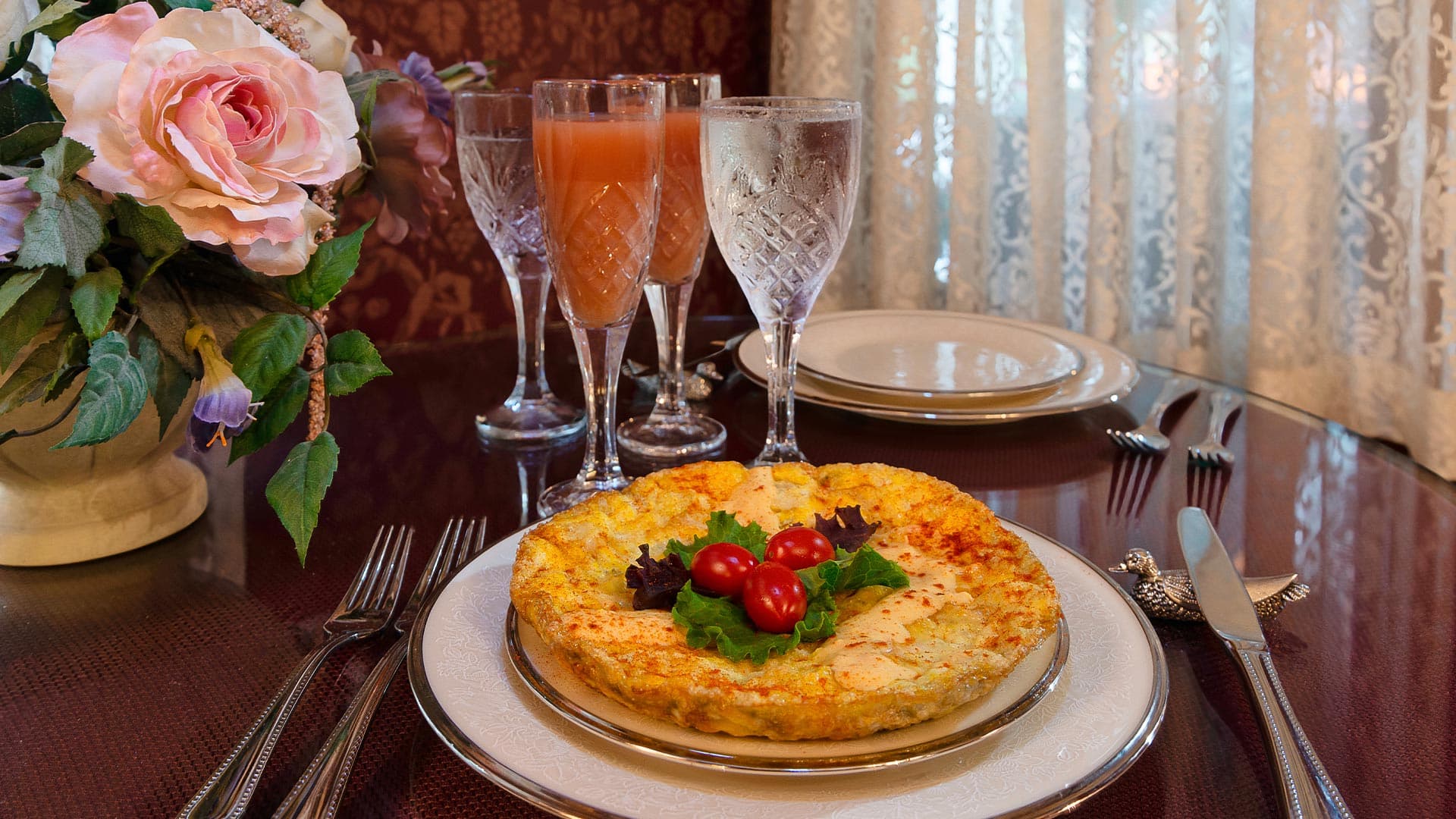 A beautifully arranged table featuring a savory dish garnished with greens and cherry tomatoes, alongside elegant glasses of beverages.