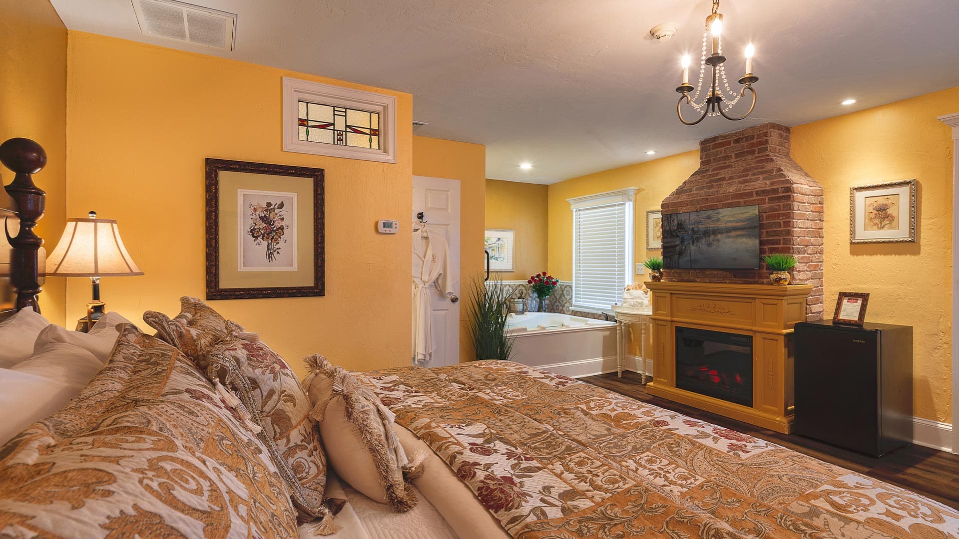 Cozy bedroom featuring yellow walls, ornate bedding, a fireplace, and an en-suite bathroom.