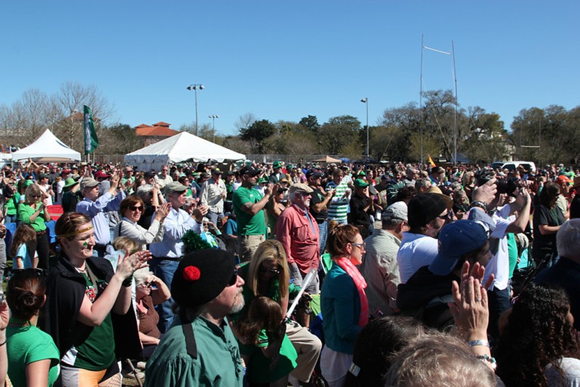 Crowd of people at Celtic Music & Heritage Festival with two white tent tops and trees in background blue sky