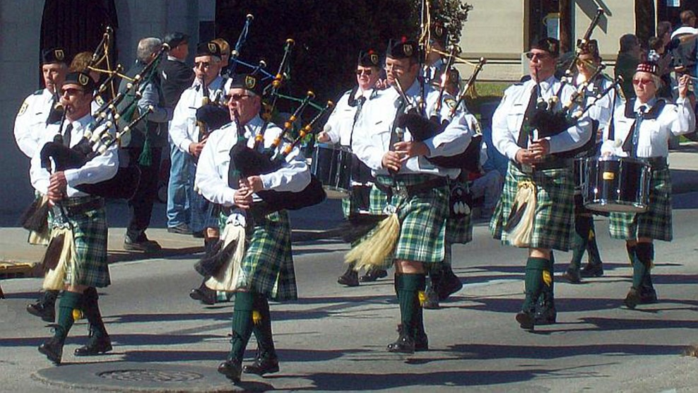 Bagpipers wearing green and black plaid kilts, white shirts, green socks playing in St Patricks Day Parade