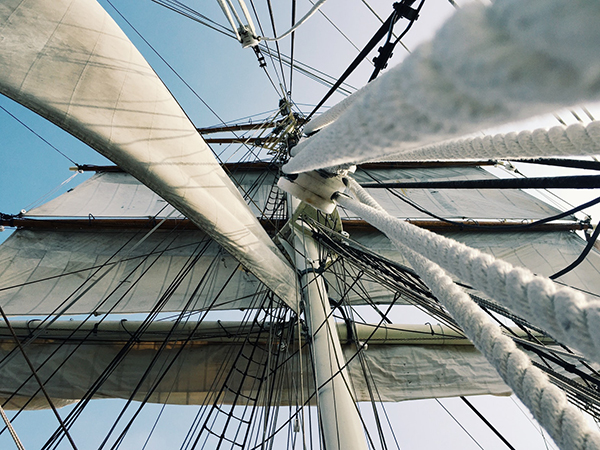 View looking up into mast, rigging, white sails of schooner against clear blue sky