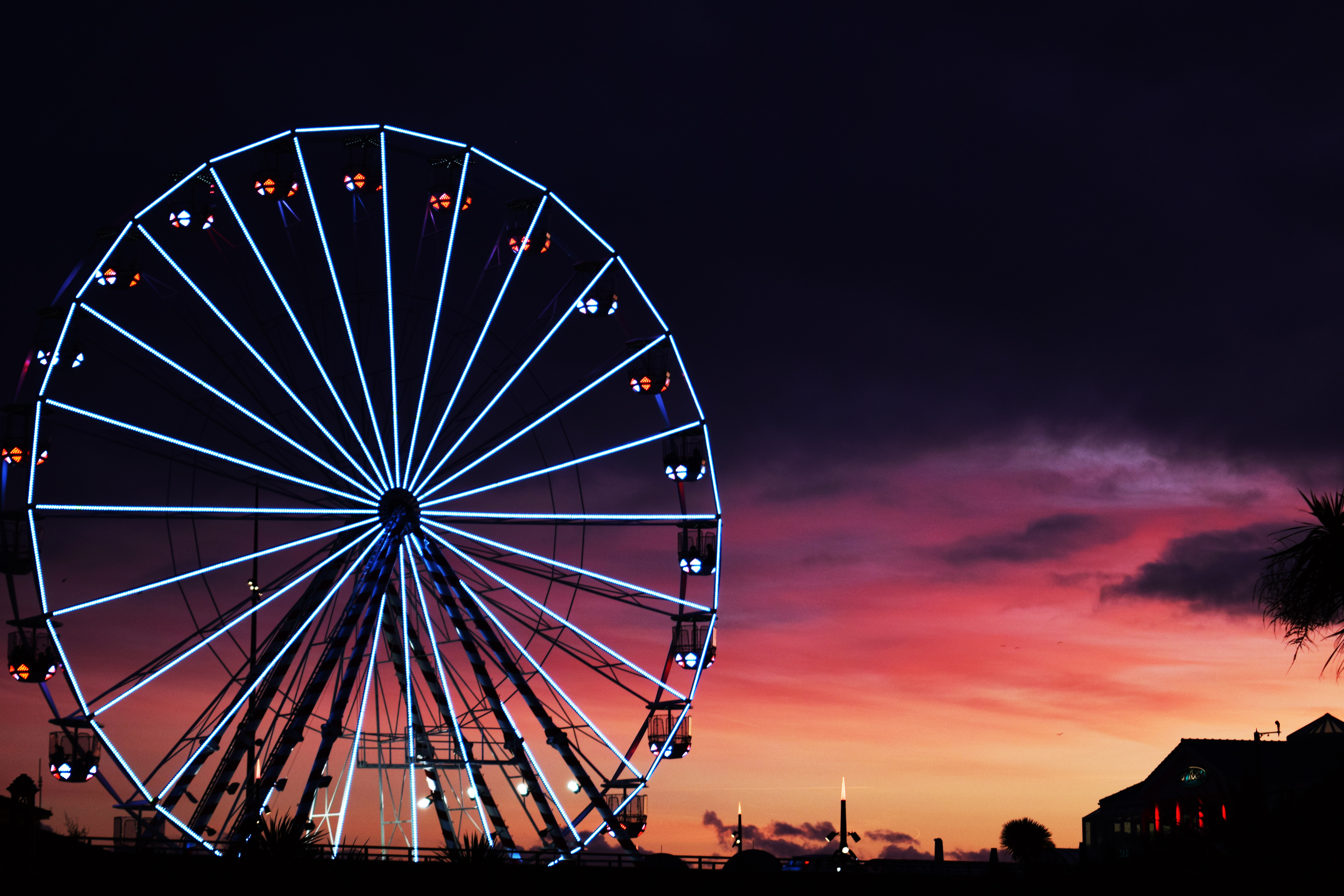 A Ferris wheel with blue lights in front of a pink and orange sunset.