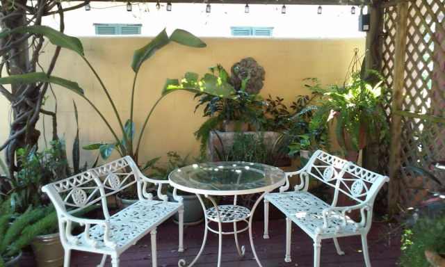 two white wrought iron seats and a table on enclosed patio with green plants