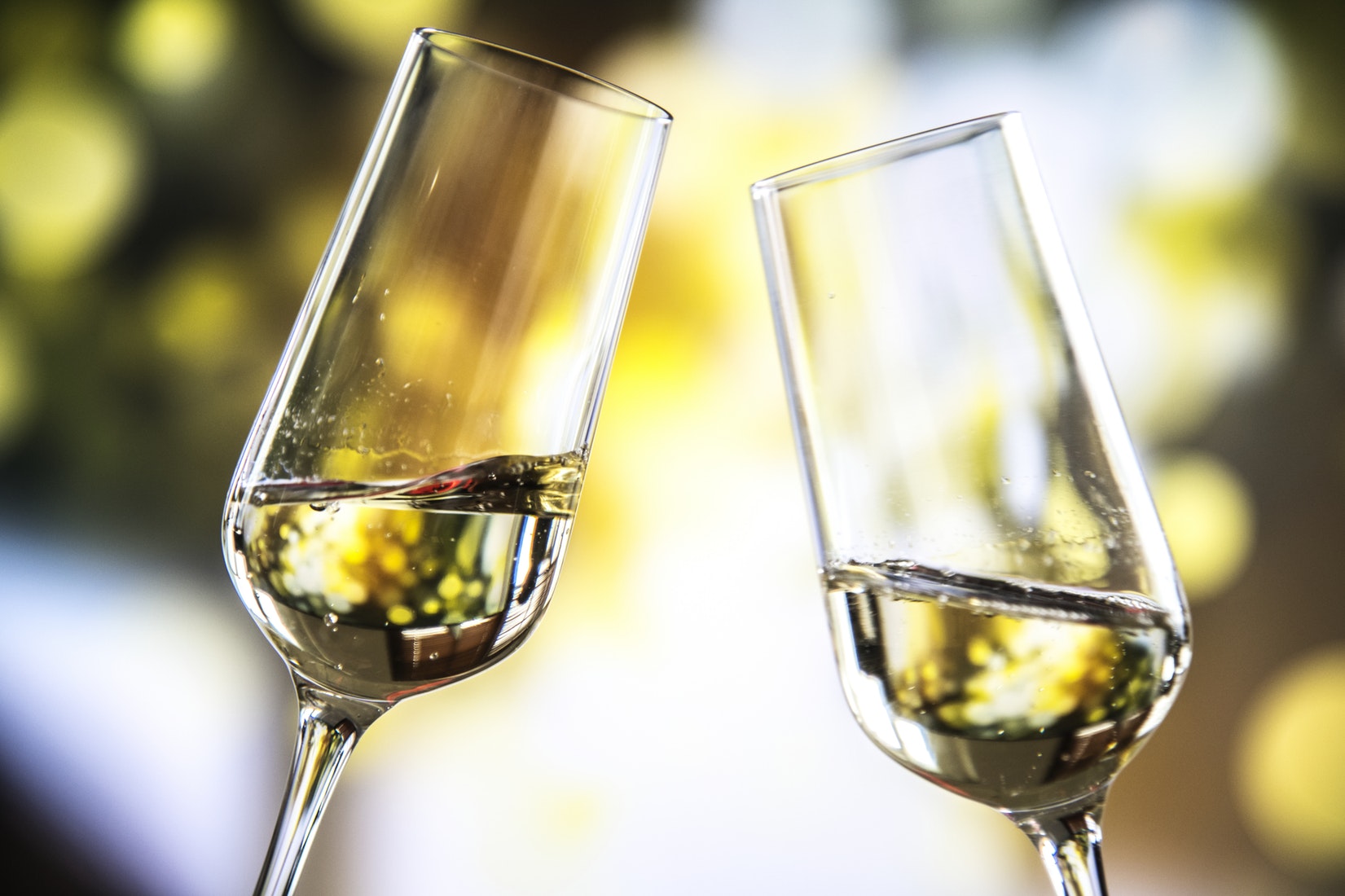 two glass flutes with sparkling gold wine being held against each other in toast