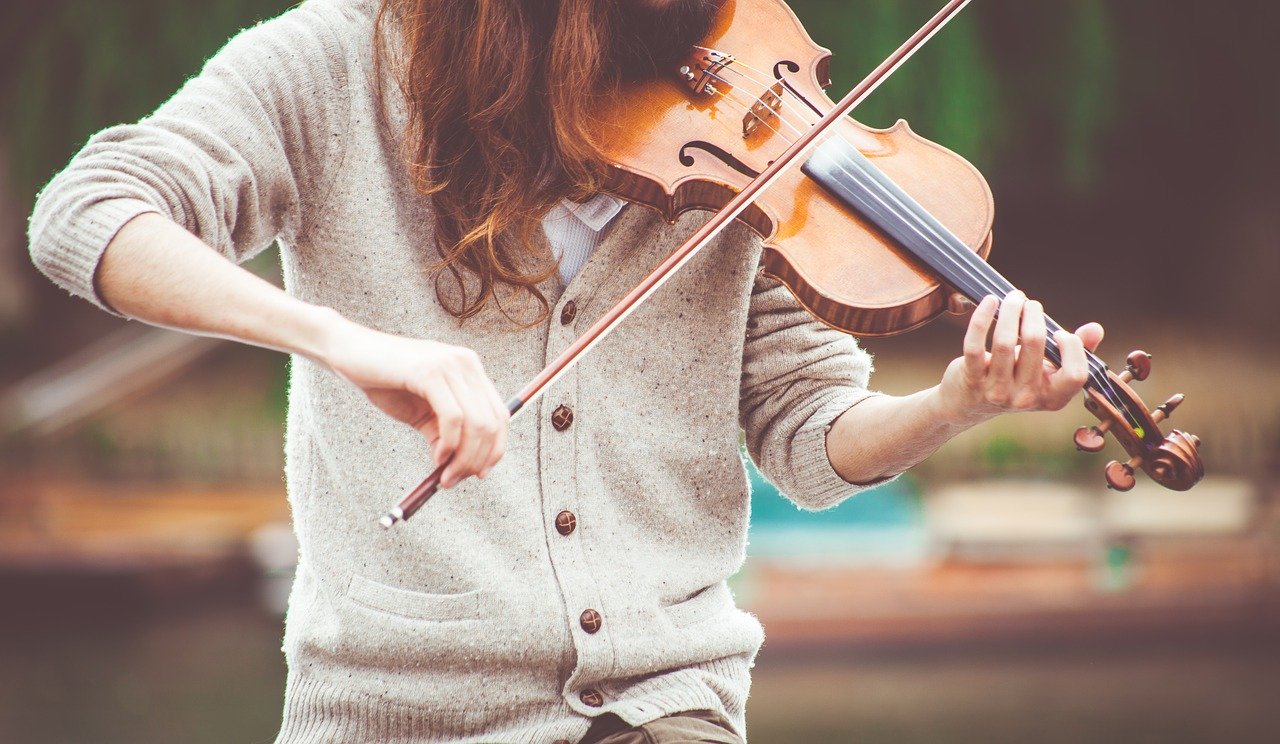 A woman in a button-down cardigan playing a violin outside.